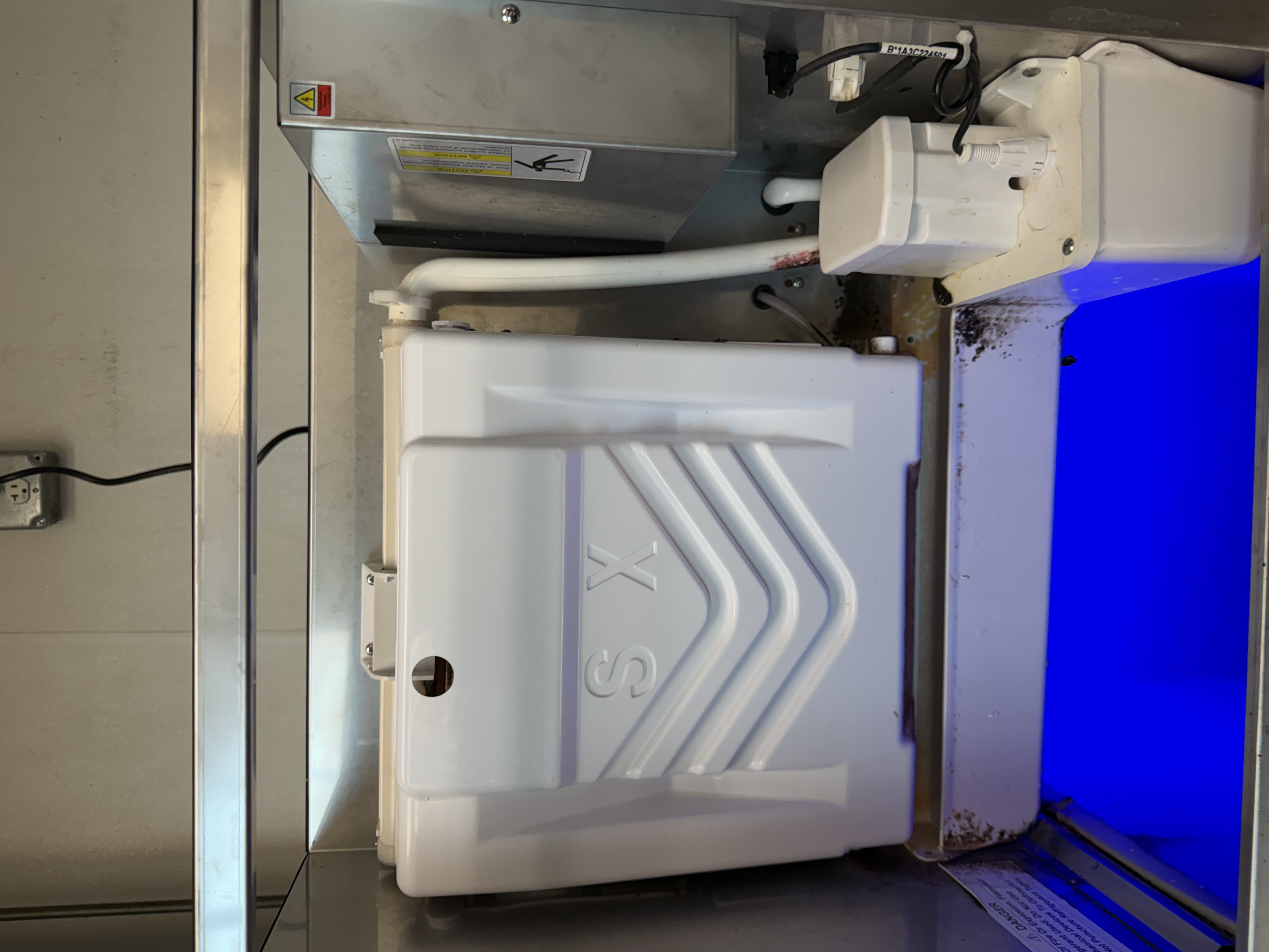 Commercial ice machine top cabinet opened up before cleaning, showing multiple dirty internal components